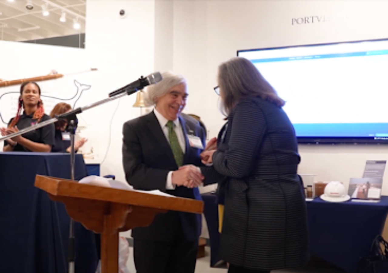 Ernest Moniz receiving the Award from Sarah Howell while at the podium.